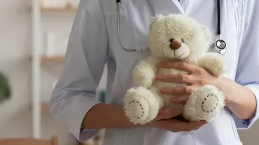Personne en blouse blanche tenant un ours en peluche.