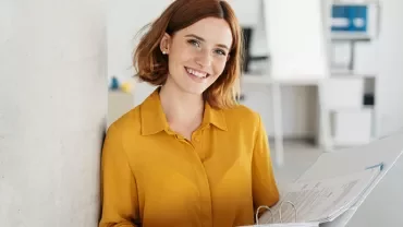 Personne souriante tenant des dossiers dans un bureau moderne.