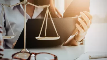 Personne lisant un dossier à côté d'une balance de justice sur un bureau.