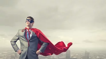 Homme en costume avec cape rouge et masque, debout sur un toit.