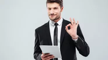 Person in suit holding tablet and showing OK gesture.