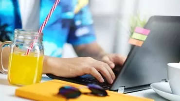 Personne tapant sur un ordinateur portable avec un verre de jus d'orange à côté.