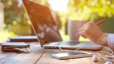 Personne travaillant sur un ordinateur portable à l'extérieur avec des écouteurs et un téléphone sur la table.