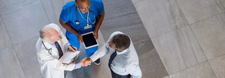 Deux médecins et un homme d'affaires se serrant la main dans un couloir.