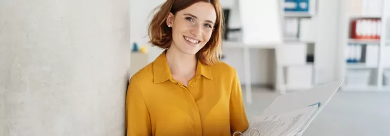 Personne souriante tenant des dossiers dans un bureau moderne.